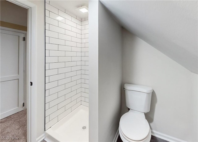 bathroom featuring lofted ceiling, toilet, and a tile shower