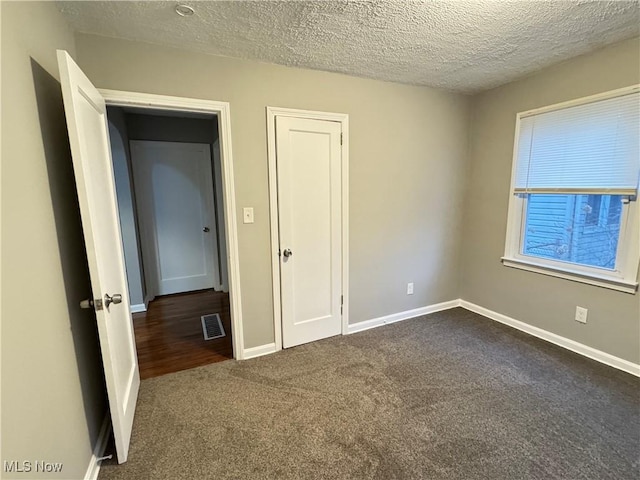 unfurnished bedroom with dark carpet and a textured ceiling