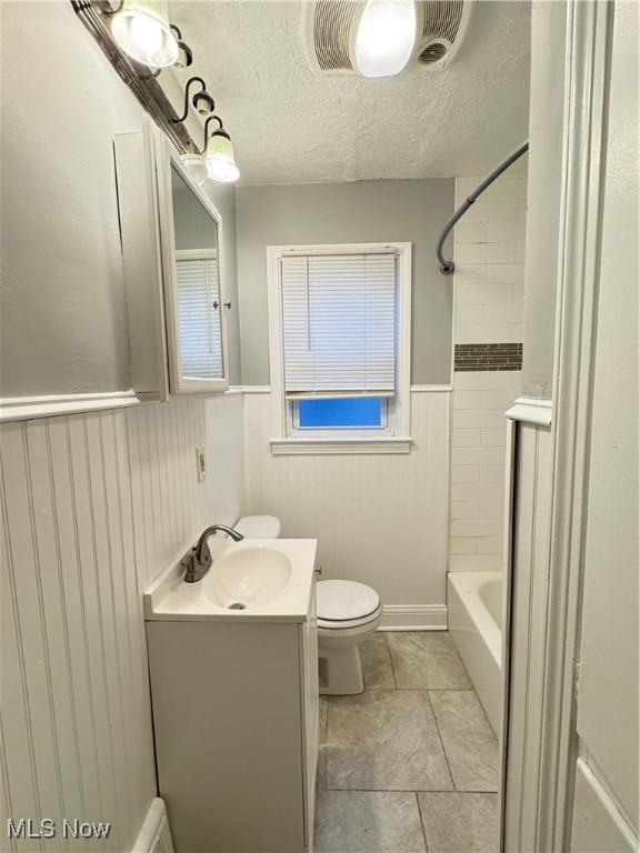 full bathroom featuring tile patterned flooring, vanity, a textured ceiling, toilet, and tiled shower / bath