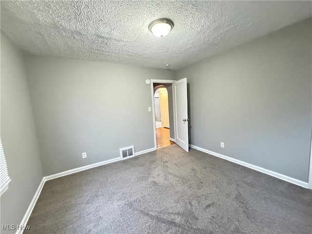 spare room with dark carpet and a textured ceiling