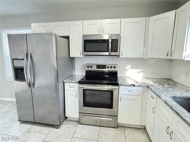 kitchen featuring light stone counters, light tile patterned floors, appliances with stainless steel finishes, white cabinets, and backsplash