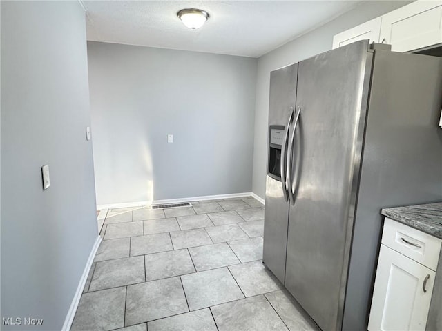 kitchen with white cabinetry, light tile patterned flooring, stainless steel fridge, and dark stone counters