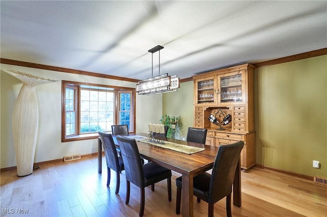 dining area with crown molding, an inviting chandelier, and light hardwood / wood-style floors