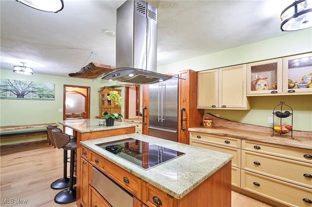 kitchen with a kitchen island, light hardwood / wood-style floors, black electric cooktop, island exhaust hood, and a kitchen breakfast bar