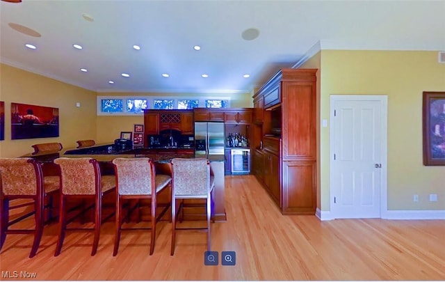 kitchen featuring light hardwood / wood-style floors, crown molding, a breakfast bar area, and stainless steel fridge