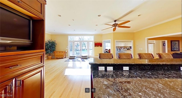 kitchen with light wood-type flooring, ceiling fan, dark stone counters, a kitchen bar, and crown molding