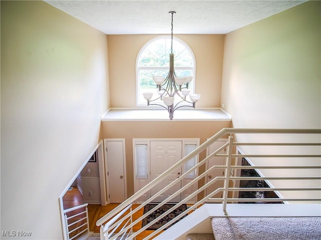 staircase with a textured ceiling, wood-type flooring, and a notable chandelier