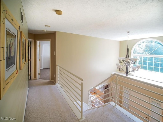 hallway with a textured ceiling, light colored carpet, and a notable chandelier