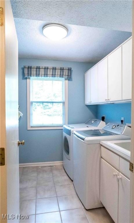 laundry area featuring light tile patterned flooring, washer and dryer, cabinets, and a textured ceiling