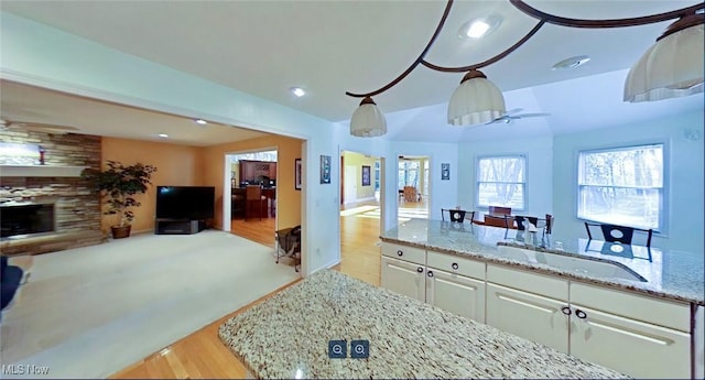 kitchen featuring a fireplace, hanging light fixtures, light stone countertops, sink, and white cabinets