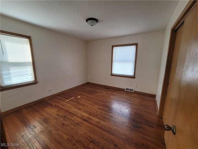 empty room featuring a wealth of natural light and dark wood-type flooring