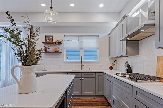 kitchen featuring sink, wall chimney range hood, gray cabinetry, and pendant lighting