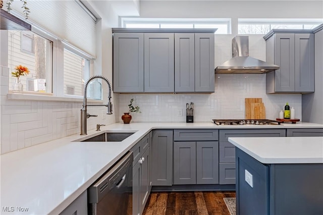 kitchen with gray cabinetry, wall chimney exhaust hood, stainless steel gas stovetop, sink, and black dishwasher