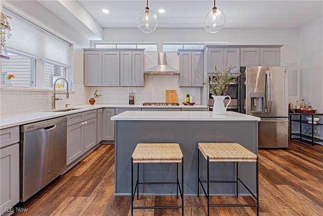 kitchen with a center island, wall chimney range hood, stainless steel appliances, and decorative light fixtures