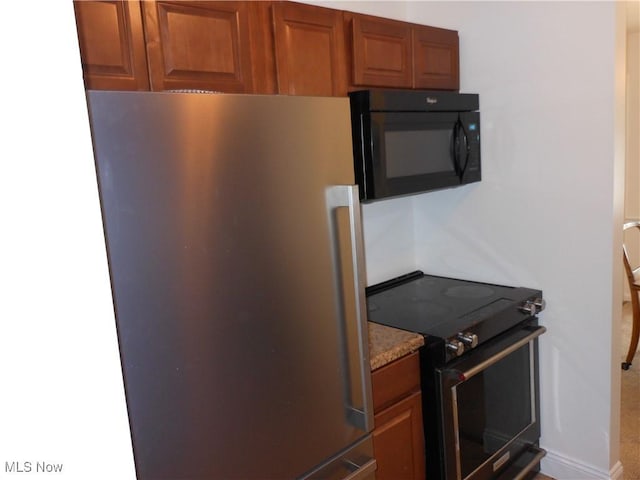 kitchen featuring stainless steel refrigerator, electric stove, and light stone countertops