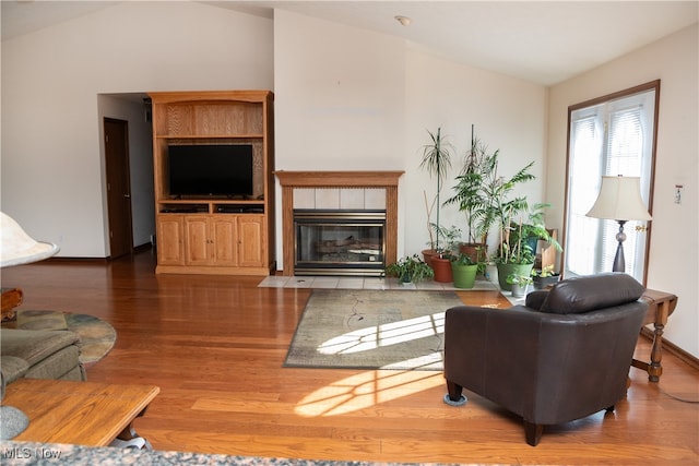living room with vaulted ceiling, wood-type flooring, and a tiled fireplace