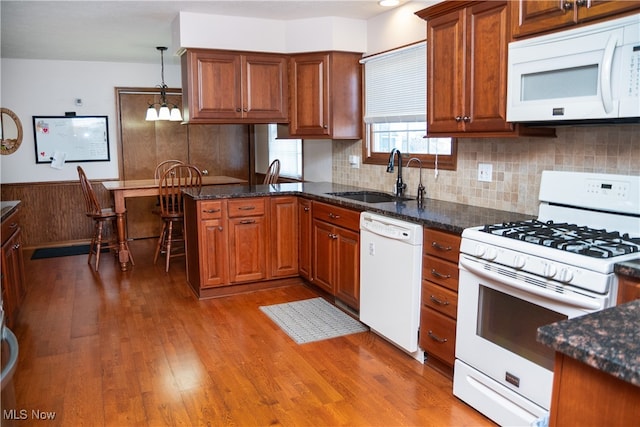 kitchen featuring wood-type flooring, white appliances, pendant lighting, sink, and dark stone countertops