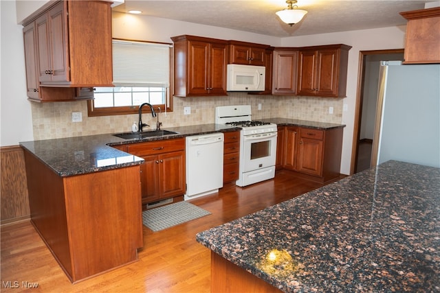 kitchen featuring white appliances, dark stone countertops, sink, light hardwood / wood-style floors, and kitchen peninsula