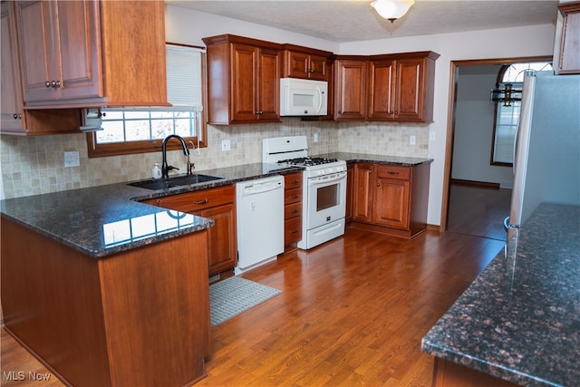 kitchen with sink, backsplash, white appliances, dark stone counters, and dark wood-type flooring