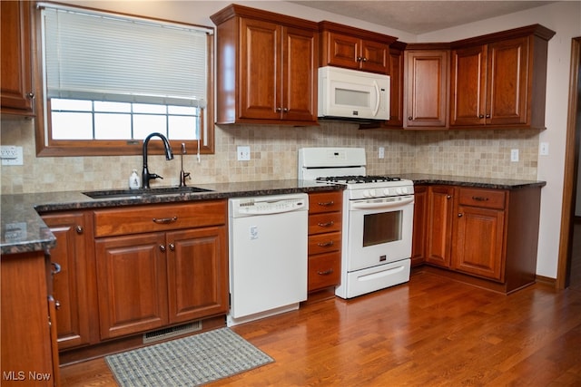 kitchen featuring white appliances, dark stone countertops, sink, dark hardwood / wood-style floors, and tasteful backsplash