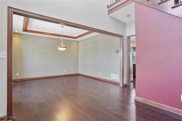 empty room with a raised ceiling, dark wood-type flooring, and ornamental molding