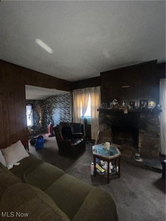 living room featuring a stone fireplace, carpet floors, and wooden walls