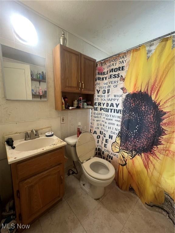 bathroom with tile walls, curtained shower, vanity, tile patterned flooring, and toilet