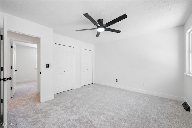 unfurnished bedroom featuring a textured ceiling, ceiling fan, light colored carpet, and two closets