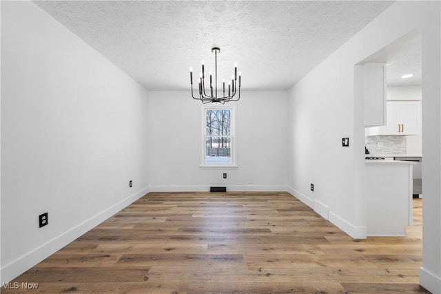 unfurnished dining area with a textured ceiling, an inviting chandelier, and light hardwood / wood-style floors