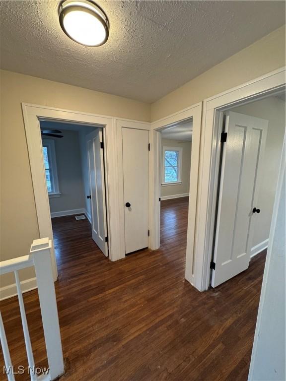 corridor with a textured ceiling and dark wood-type flooring