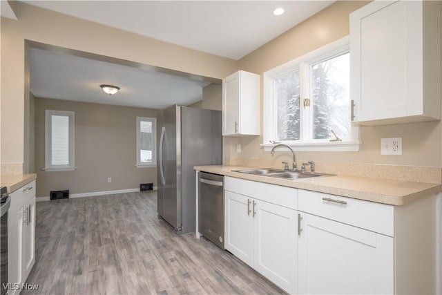 kitchen with appliances with stainless steel finishes, sink, white cabinets, and light hardwood / wood-style floors