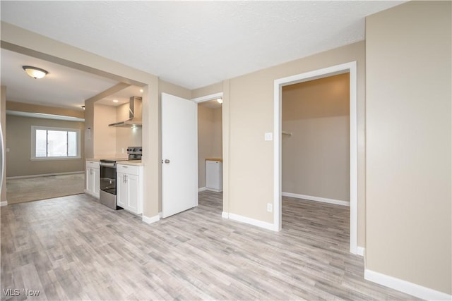 kitchen featuring light wood-type flooring, stainless steel electric range, wall chimney range hood, and white cabinets