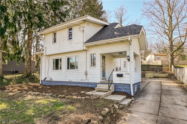 view of front of house featuring roof with shingles, driveway, and fence