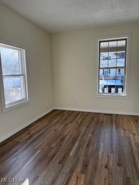 empty room featuring dark hardwood / wood-style flooring, a textured ceiling, and a wealth of natural light