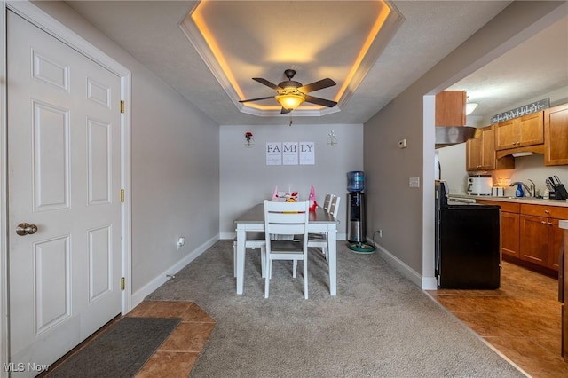 carpeted dining room with ceiling fan and a raised ceiling