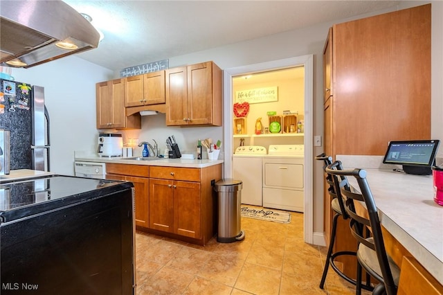 kitchen featuring sink, island exhaust hood, washing machine and clothes dryer, light tile patterned flooring, and stainless steel fridge