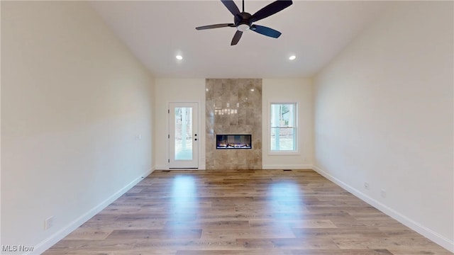 unfurnished living room featuring a tile fireplace, light wood-type flooring, vaulted ceiling, and ceiling fan