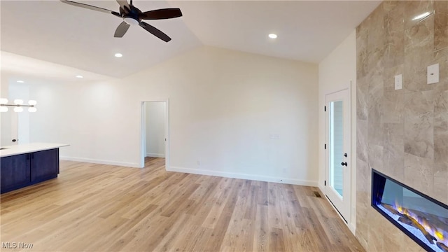 unfurnished living room with light wood-type flooring, ceiling fan, vaulted ceiling, and a fireplace