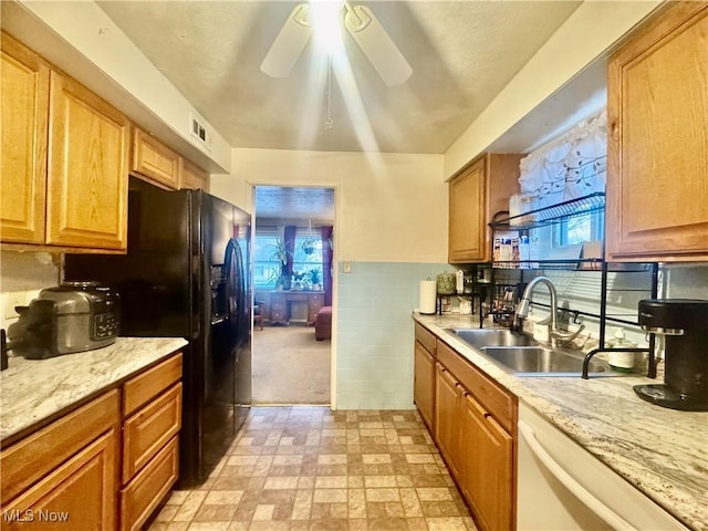 kitchen with light stone counters, tile walls, ceiling fan, sink, and white dishwasher