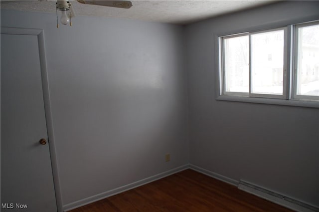 spare room with dark wood-style floors, baseboard heating, ceiling fan, a textured ceiling, and baseboards