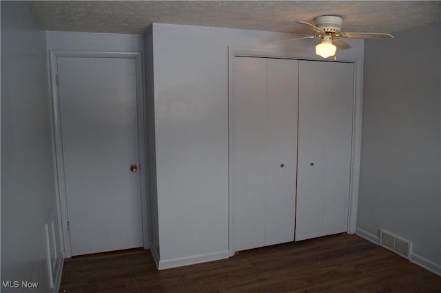 unfurnished bedroom with visible vents, ceiling fan, dark wood-type flooring, a textured ceiling, and a closet