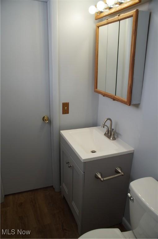 half bath featuring toilet, wood finished floors, and vanity