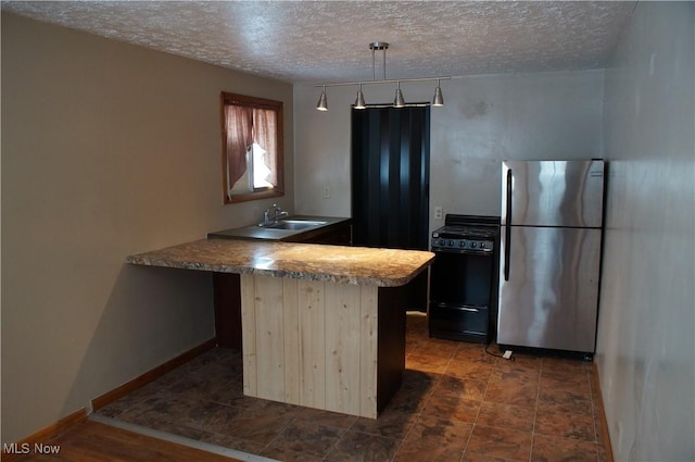 kitchen with a textured ceiling, black gas range, a peninsula, freestanding refrigerator, and pendant lighting