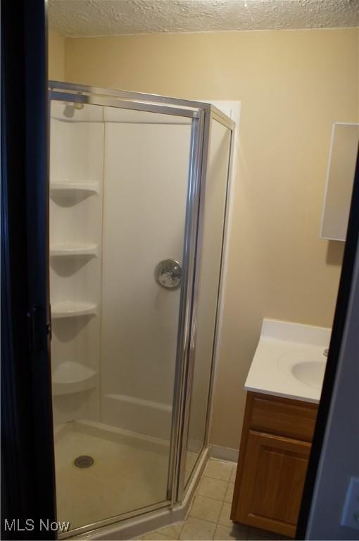 full bath featuring a textured ceiling, a stall shower, tile patterned flooring, and vanity