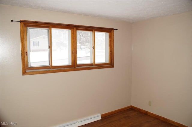 empty room featuring dark wood-style floors, a baseboard heating unit, a textured ceiling, and baseboards