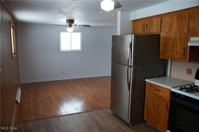 kitchen featuring under cabinet range hood, dark wood-style flooring, light countertops, tasteful backsplash, and gas stove