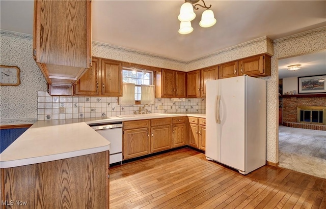 kitchen with white appliances, sink, light wood-type flooring, kitchen peninsula, and a fireplace