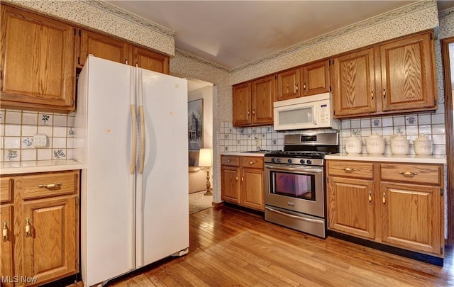 kitchen with light wood-type flooring, ornamental molding, white appliances, and tasteful backsplash