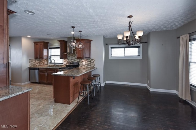 kitchen with stainless steel appliances, an inviting chandelier, wall chimney range hood, a kitchen breakfast bar, and pendant lighting