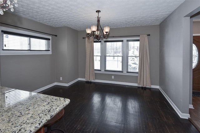 unfurnished dining area featuring a textured ceiling, a chandelier, and dark hardwood / wood-style floors